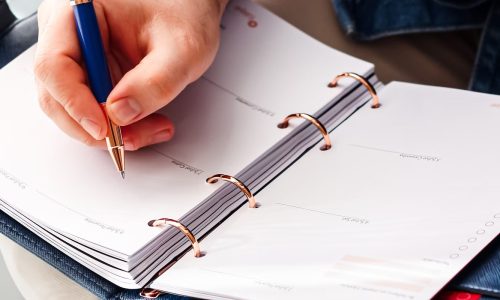 Hand die met een pen aantekeningen maakt in een planner